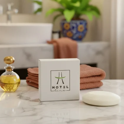 Saponetta linea cortesia Hotel Line in scatola di cartoncino bianco e sapone nudo tondo su ripiano in marmo, con asciugamani color ruggine e flacone di olio profumato in un bagno moderno