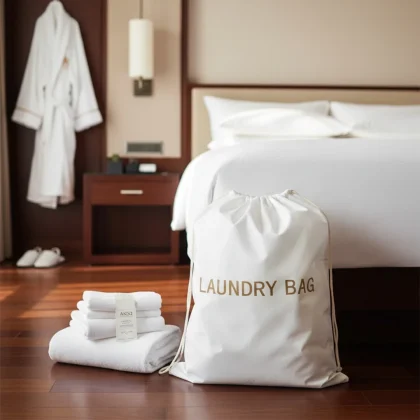 Sacco lavanderia hotel premium in TNT bianco formato grande 56x48cm, con scritta Laundry Bag, ambientato in una suite di lusso accanto al letto.