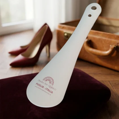 Calzascarpe professionale per hotel in plastica bianca personalizzato con logo a colori Dimora San Quirico Puglia Italia, appoggiato su cuscino di velluto.