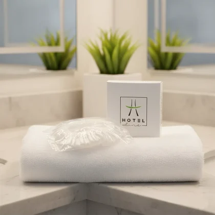 Cuffia doccia per hotel linea Hotel Line in scatolina di cartoncino bianco con finitura opaca soft-touch, appoggiata su un asciugamano bianco in un bagno di design.