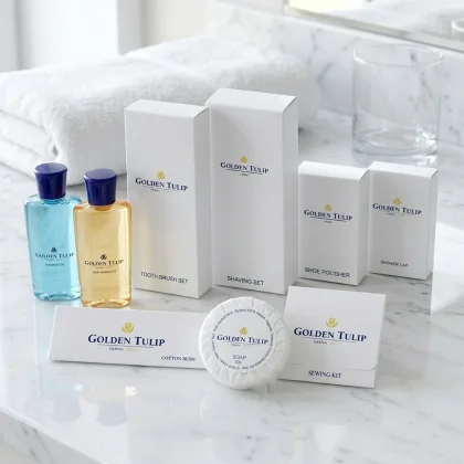 Kit benvenuto hotel linea Crystal White con flaconi trasparenti, saponetta e scatoline bianche su marmo bianco e asciugamano sullo sfondo.