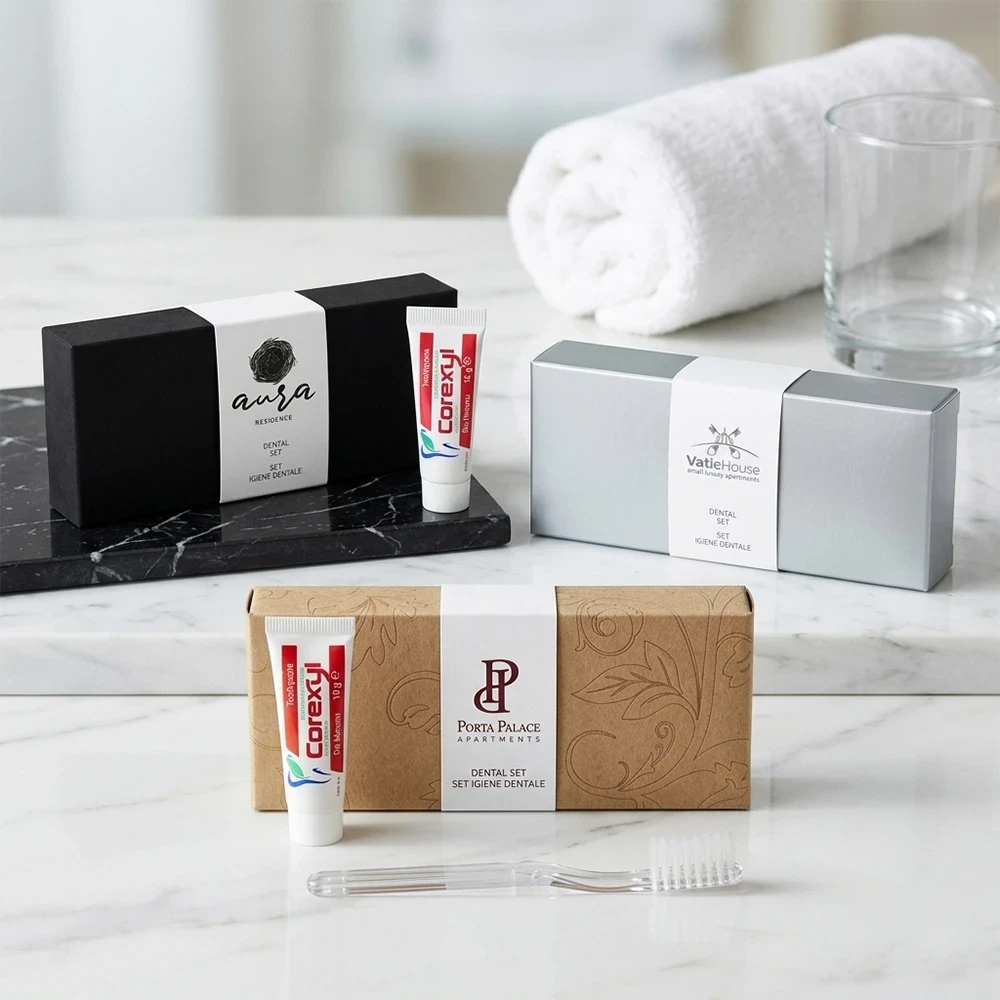 Tre modelli di kit igiene orale hotel con fascetta bianca personalizzata su basi nero soft-touch, argento e kraft con spazzolino trasparente e dentifricio Corexyl.