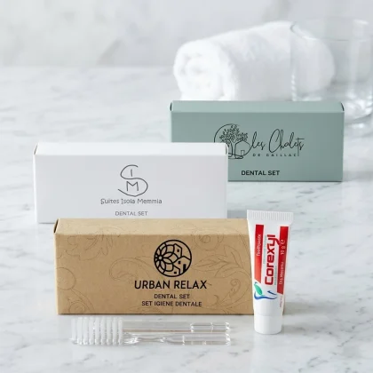 Tre modelli di scatoline per kit igiene orale hotel: bianco Suites Isola Memmia, kraft Urban Relax e azzurro Les Chalets con spazzolino trasparente e dentifricio Corexyl su marmo