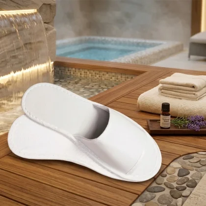 Pantofole bianche specifiche per SPA e piscina, resistenti all'acqua, appoggiate su un bordo in legno accanto a una cascata d'acqua e un idromassaggio.