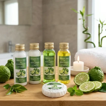 Set cortesia hotel in pronta consegna con flaconi da 30ml al tè verde e bergamotto, saponetta, candela e foglie di tè su vassoio in legno.